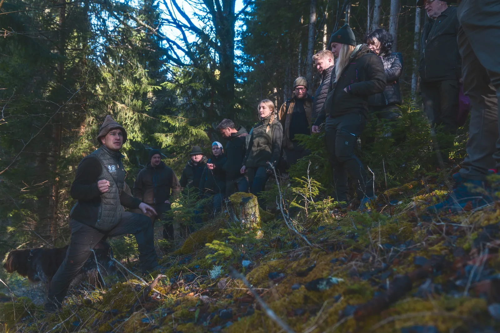 Jagdkurs-Gruppe mit Kursleiter und Jagdhund am bemoosten Waldhang beim Forsttag, Jagdkurs Leoben, Reportagefoto in natürlichem Licht